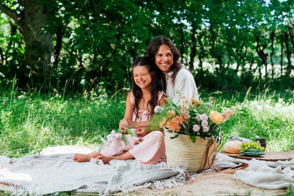 smilende mor og datter på skovtur med smukke blomster i stråtaske